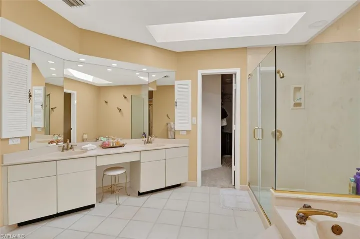 Bathroom with a skylight, double vanity, a stall shower, a bath, and light tile patterned flooring