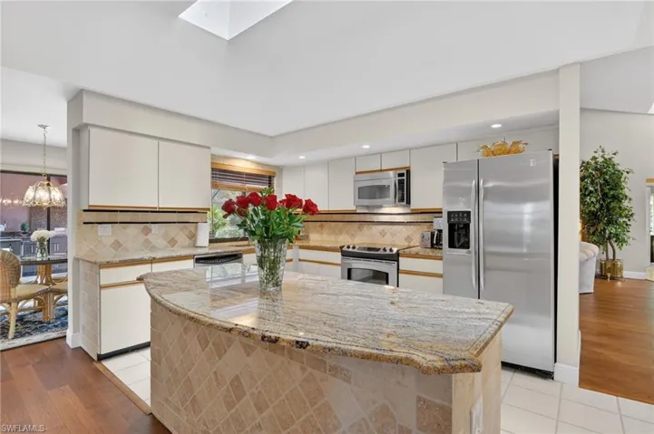 Dual tone kitchen with stainless steel appliances, backsplash, light stone countertops, a center island, and a skylight