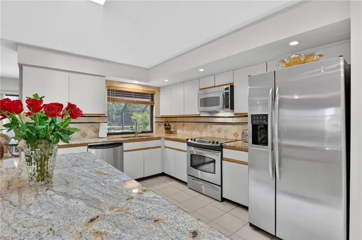 Kitchen featuring stainless steel appliances, backsplash, light tile patterned floors, light stone counters, and recessed lighting