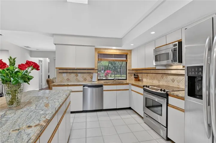 Kitchen featuring stainless steel appliances, decorative backsplash, two tone cabinets, light stone countertops, and light tile patterned floors