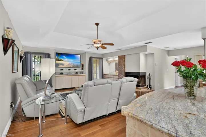 Living area with light wood-style flooring, ceiling fan, a fireplace, and a raised ceiling