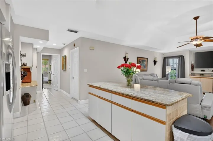 Two tone kitchen with light stone countertops, stainless steel refrigerator with ice dispenser, ceiling fan, open floor plan, and two tone color scheme