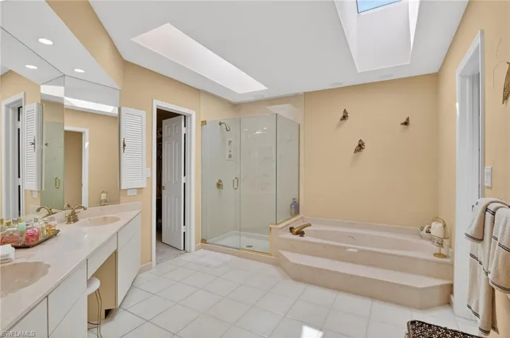 Full bath with a skylight, double vanity, a shower stall, a garden tub, and light tile patterned flooring