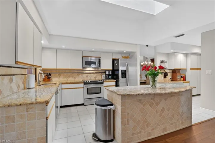 Kitchen featuring light stone countertops, stainless steel appliances, white cabinets, a kitchen island, and suspended lighting