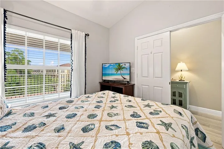 Vaulted ceiling, large window with blinds, wood-finish flooring, and a built-in closet with bifold doors