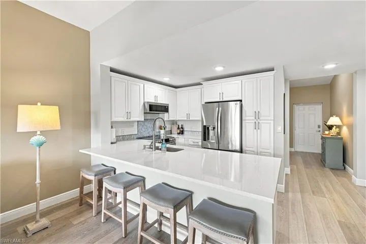 White cabinetry, stainless steel appliances, light-toned wood-finish flooring, recessed lighting, and a white countertop with a breakfast bar