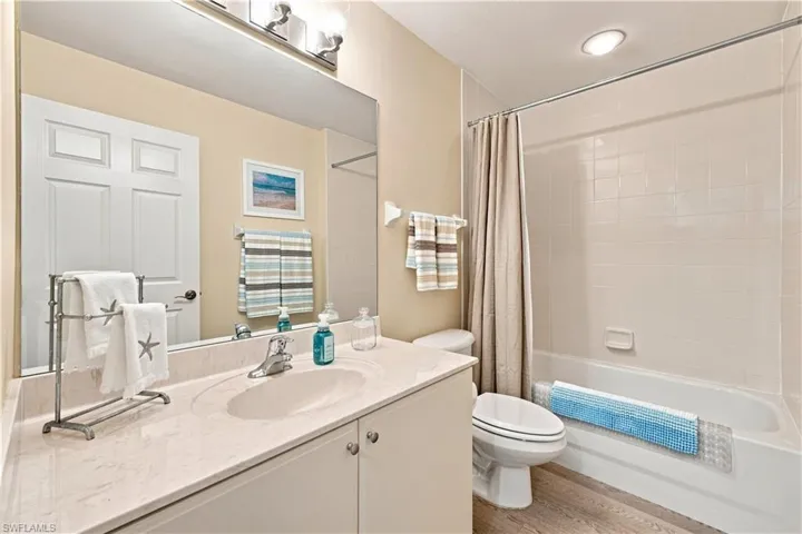 Bathroom featuring a vanity with an integrated sink, a full-width mirror, a shower-tub combination with tiled surround, and wood-finish flooring