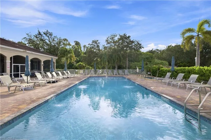 Expansive swimming pool with integrated water features, bordered by a paver deck, a covered lanai, and lush landscaping