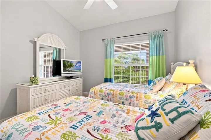 Vaulted ceiling, ceiling fan, window with blinds, white dresser with mirror, and white bed frames