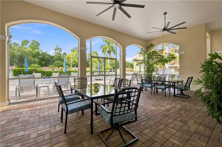 Covered patio featuring brick paver flooring, multiple ceiling fans, arched openings, and screened enclosures