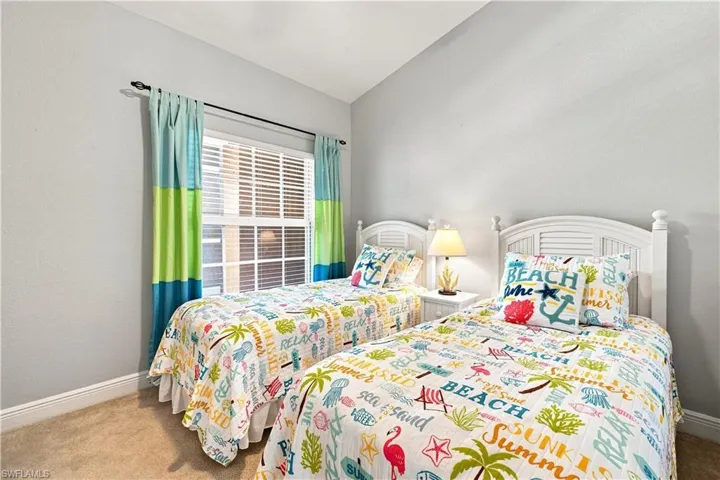 Carpeted room with a window featuring blinds and colorful drapes, accompanied by two white headboards