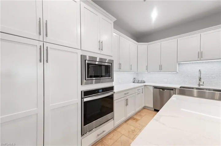 Kitchen featuring stainless steel appliances, white cabinets, light stone counters, and tasteful backsplash