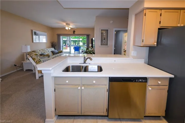 Kitchen featuring dishwasher, sink, kitchen peninsula, light colored carpet, and light brown cabinetry