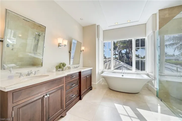 Bathroom featuring double vanity, a freestanding tub, a shower stall, light tile patterned floors, and recessed lighting