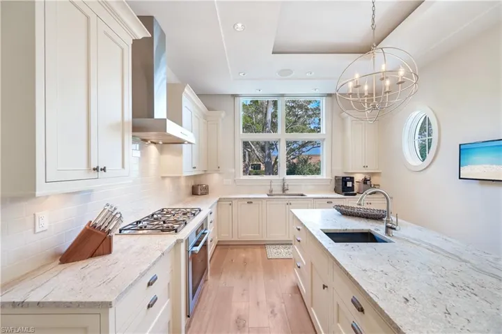 Kitchen with light stone countertops, light wood-style floors, stainless steel appliances, suspended lighting, and decorative backsplash