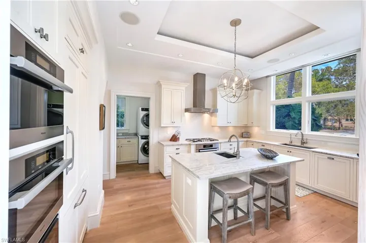 Kitchen featuring stainless steel appliances, light wood-style floors, hanging lights, white cabinets, and a tray ceiling