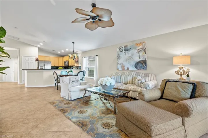 Tiled living room with ceiling fan with notable chandelier and lofted ceiling