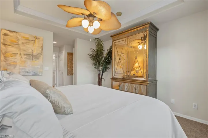 Carpeted bedroom with ceiling fan, a raised ceiling, and ornamental molding