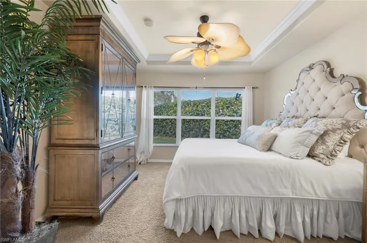 Bedroom featuring ceiling fan, crown molding, light carpet, and a tray ceiling