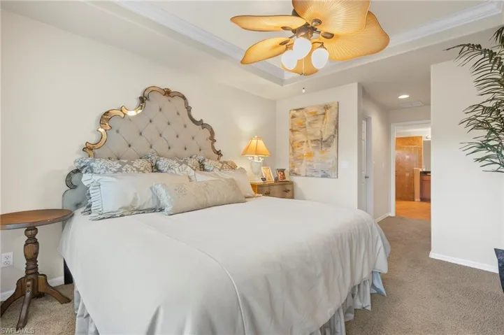 Carpeted bedroom featuring ceiling fan, a raised ceiling, crown molding, and connected bathroom
