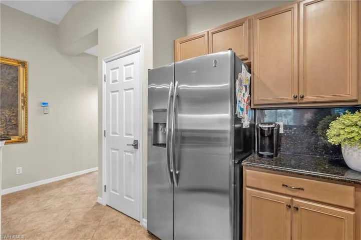 Kitchen featuring stainless steel fridge, dark stone countertops, backsplash, and light tile patterned flooring