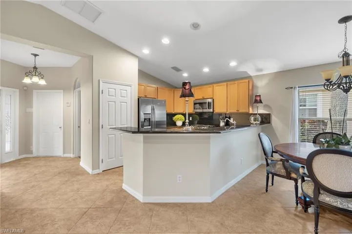 Kitchen featuring decorative backsplash, stainless steel appliances, an inviting chandelier, hanging light fixtures, and lofted ceiling