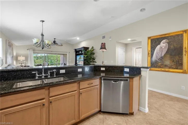Kitchen featuring stainless steel dishwasher, a notable chandelier, dark stone countertops, and sink