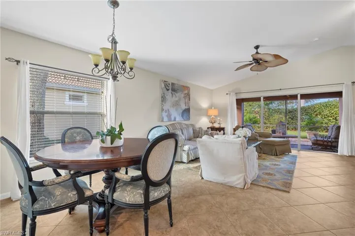 Dining room featuring light tile patterned floors, ceiling fan with notable chandelier, and lofted ceiling