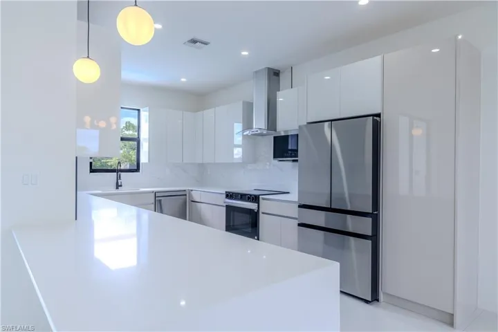 Kitchen with stainless steel appliances, hanging light fixtures, a peninsula, modern cabinets, and white cabinetry