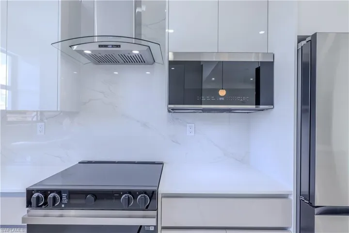 Kitchen featuring white cabinets, backsplash, modern cabinets, island range hood, and appliances with stainless steel finishes