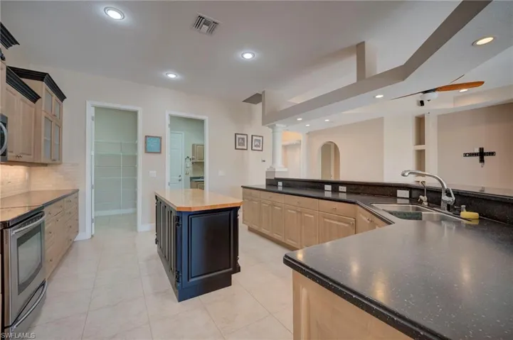 Kitchen with stainless steel range with electric cooktop, recessed lighting, light tile patterned floors, tasteful backsplash, and glass fronted cabinets