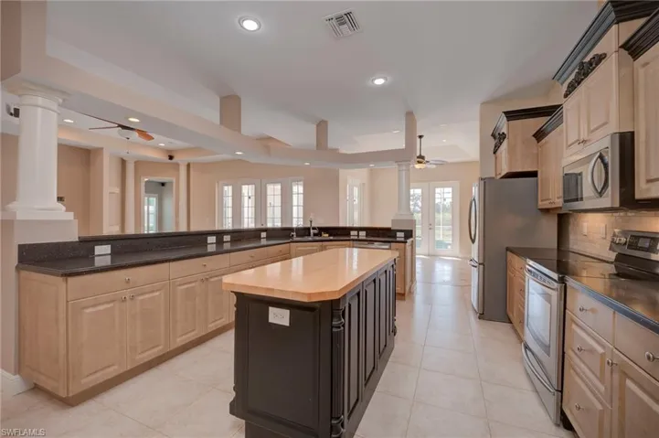 Kitchen with ceiling fan, stainless steel appliances, decorative columns, a center island, and two tone cabinets
