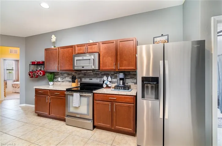 Kitchen featuring stainless steel appliances, light stone countertops, light tile flooring, and backsplash