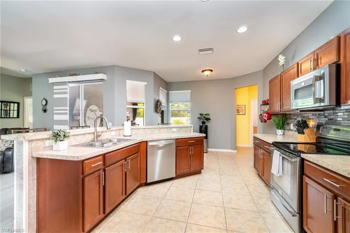 Kitchen with light stone counters, backsplash, appliances with stainless steel finishes, sink, and light tile floors