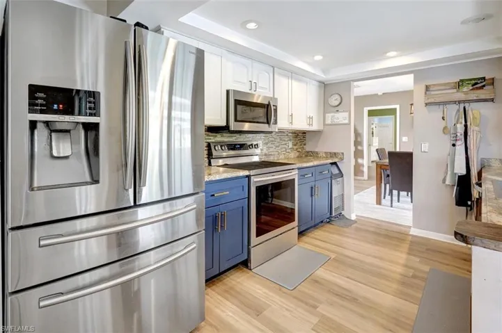 Kitchen featuring tasteful backsplash, blue cabinetry, white cabinets, light hardwood / wood-style floors, and stainless steel appliances