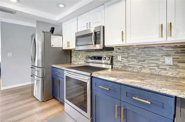 Kitchen featuring light wood-type flooring, decorative backsplash, white cabinetry, stainless steel appliances, and blue cabinetry