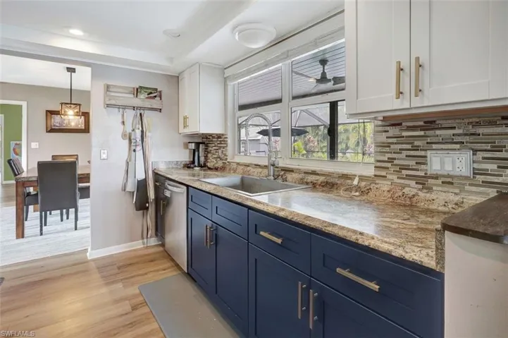 Kitchen featuring light wood-type flooring, backsplash, white cabinetry, dishwasher, and sink