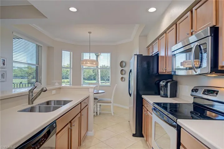 Kitchen with light countertops, a sink, appliances with stainless steel finishes, light tile patterned floors, and decorative light fixtures