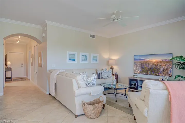 Living area featuring visible vents, ornamental molding, arched walkways, a ceiling fan, and light tile patterned floors
