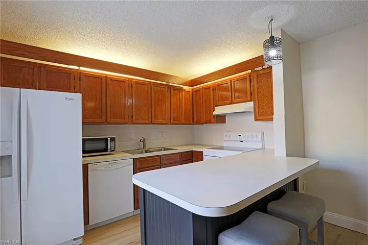 Kitchen featuring white appliances, a peninsula, a kitchen bar, light wood finished floors, and decorative light fixtures