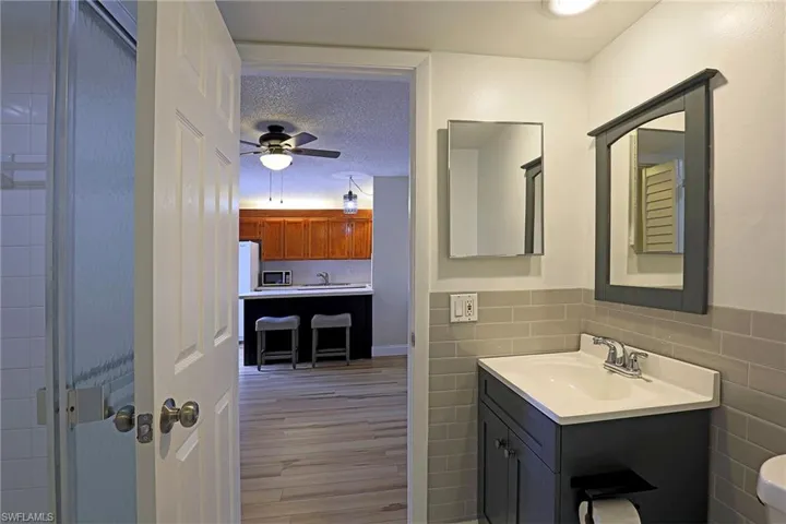 Bathroom featuring tile walls, a textured ceiling, vanity, light wood finished floors, and a wainscoted wall