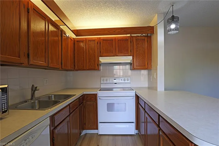 Kitchen with white appliances, tasteful backsplash, light countertops, brown cabinetry, and a textured ceiling