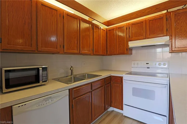 Kitchen with white appliances, backsplash, light countertops, brown cabinets, and a textured ceiling