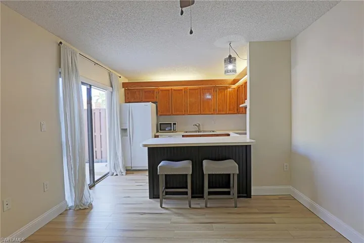 Kitchen featuring a breakfast bar area, light countertops, white fridge with ice dispenser, a peninsula, and light wood-style flooring