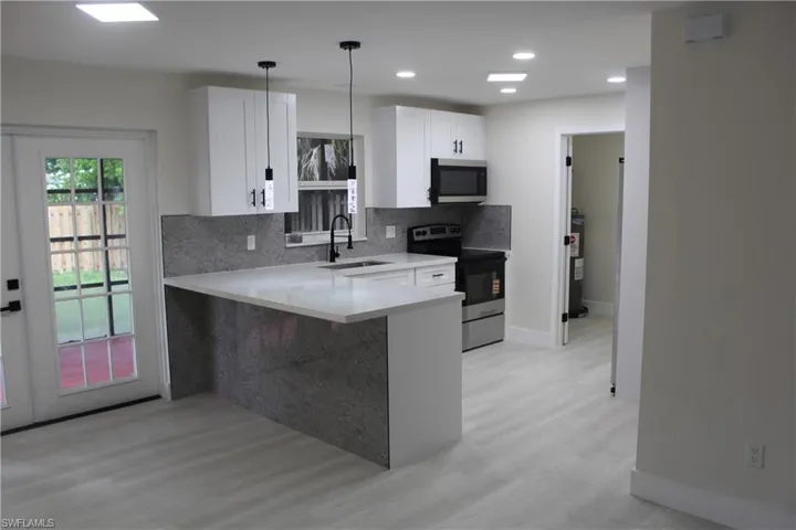 Kitchen with stainless steel appliances, decorative backsplash, light wood-style floors, light countertops, and a peninsula