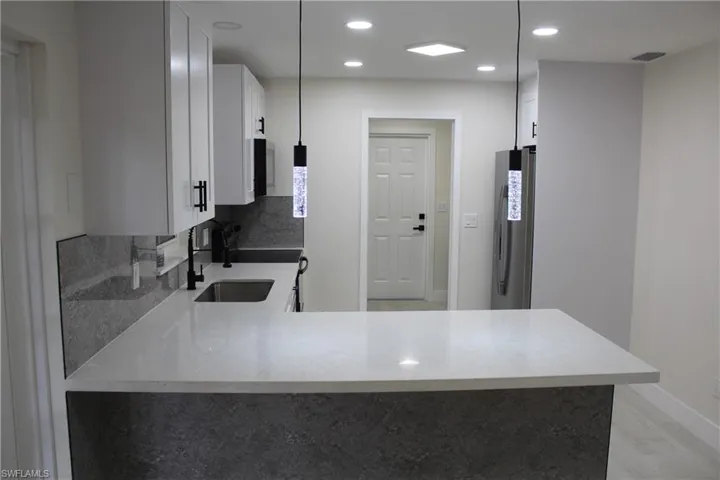 Kitchen featuring freestanding refrigerator, stove, white cabinets, a peninsula, and recessed lighting