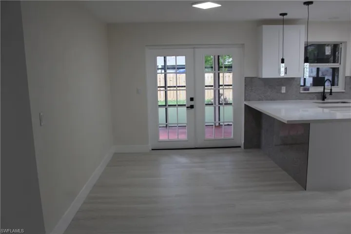 Kitchen featuring french doors, light wood-type flooring, white cabinets, light countertops, and backsplash