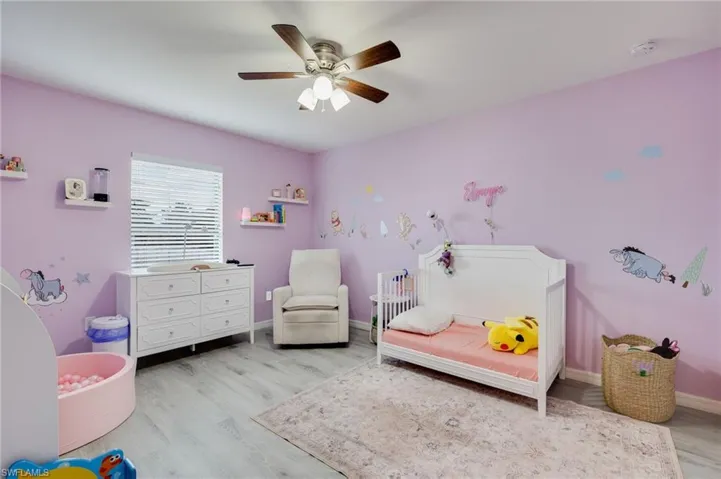 Bedroom with ceiling fan, a nursery area, and light wood-type flooring
