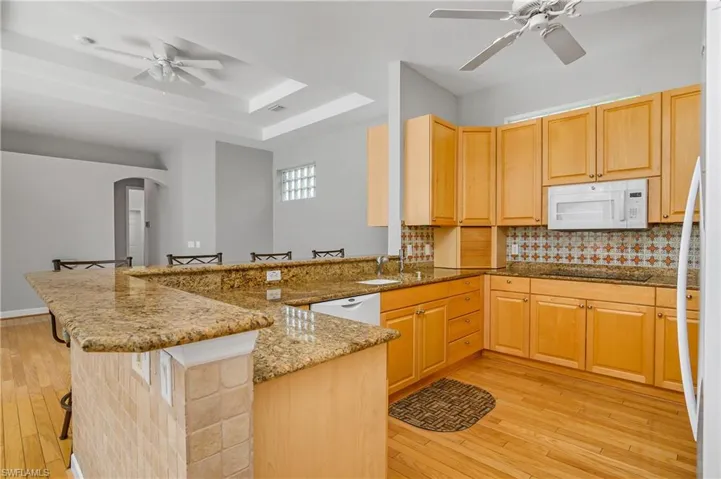 Kitchen featuring dark stone counters, backsplash, light hardwood / wood-style flooring, and white appliances