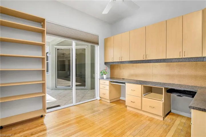 Office space featuring custom built-in desk, storage space, light hardwood / wood-style floors, and ceiling fan